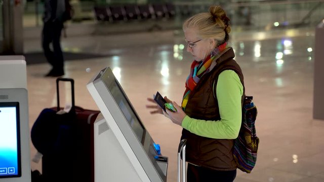 High shot of woman with passport and smartphone in hand, at an airport self check in terminal and checking herself in.