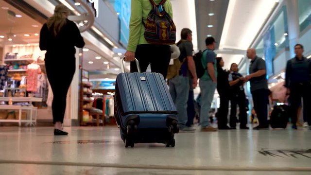 Woman’s legs and luggage as she walks through a busy airport.