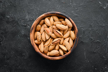 Almond nut in a bowl. Nuts on a black stone background. Top view. Free space for your text.