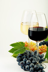 A glass of white wine, a glass of red wine, fresh grapes and grape leaves.