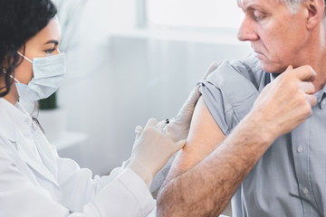 Latina doctor doing vaccination to elderly man