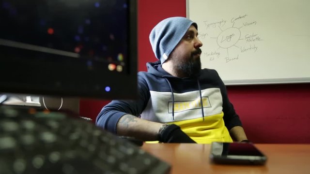 Profile of funky confident young man with hat and black gloves discussing with a flip-chart in background to colleagues in boardroom, dolling zoom view