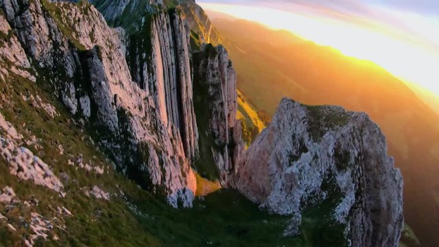 Slow motion, FPV drone shot, passing rocky, mountain peaks, over a man standing on the top of the Appenzell ridge, at sunset, in the alps of Switzerland