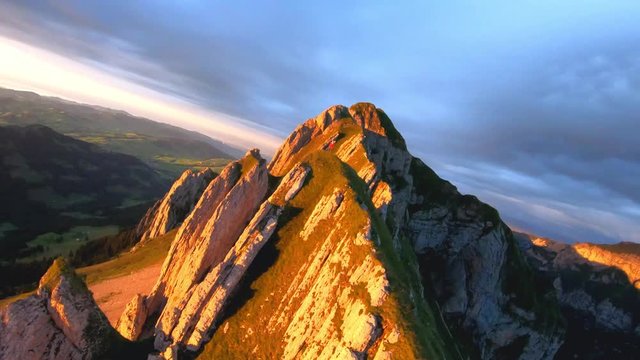 Slow motion FPV drone shot, around a man standing on the Schaefler Ridge, in the Appenzell Alps, at sunset, on a sunny summer evening, in Switzerland