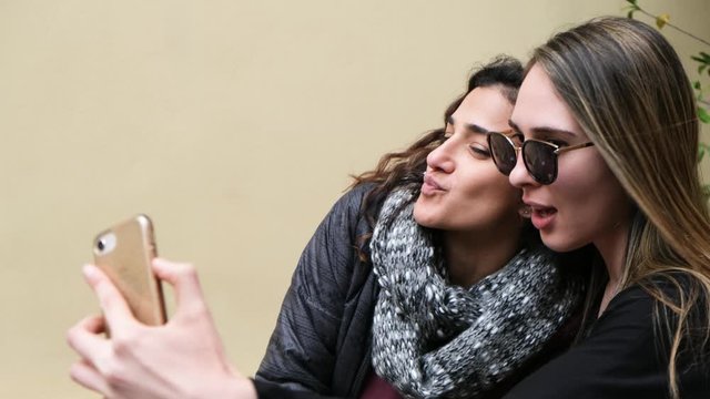 Two beautiful young girls taking a selfie with a smart phone while on a winter vacation. Both Making funny duck faces.  4k