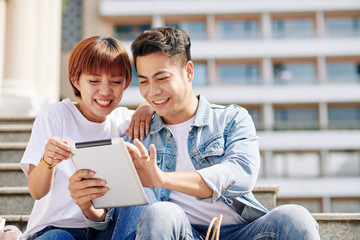 Portrait of young Asian man and woman in love spending time together outdoors watching something on tablet PC