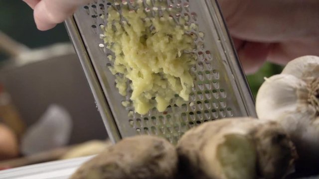 Close-up woman's hand rubs cleaned ginger root on a metal grater. Healthy Natural Food. Slow motion