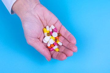 Different pills in a female hand on a blue background. Medicines. Treatment.