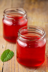 Aerial close-up of two recycled glass jars with strawberry jelly and mint leaf, on rustic wooden board, in vertical