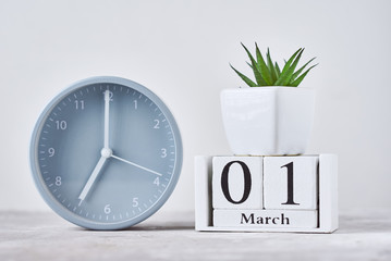 Alarm clock with wooden block calendar date 1st march and plant on the table