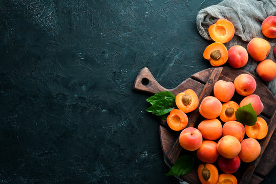 Fresh apricots with green leaves on a black background. Rustic style. Top view. Free space for your text.