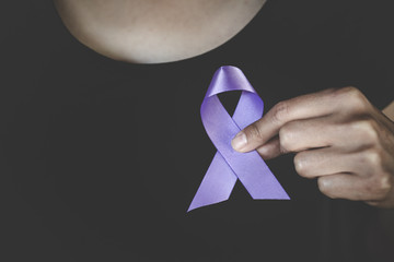 Woman Hand Holding Purple Ribbon, Domestic Violence Awareness Month (October) concept with deep purple awareness ribbon.
