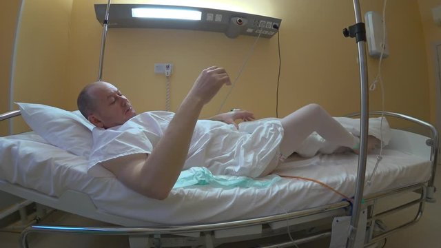 The patient entangled with tubes of drips and catheters throws back the blanket and gets up. Physical activity after laparoscopic surgery can shorten the time of rehabilitation.