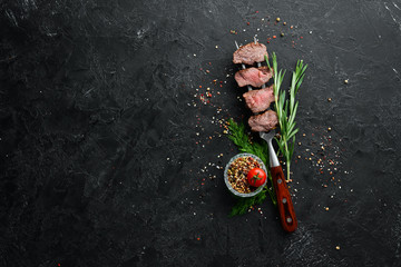 Baked veal on a fork. Veal steak on black stone background. Top view. Free space for your text.