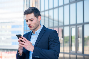 businessman standing in city looking at mobile phone