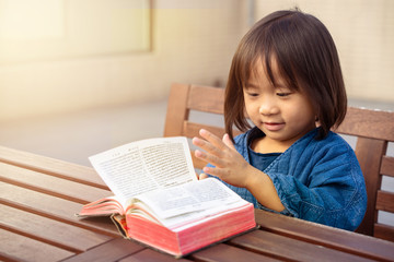 Fototapeta na wymiar Little girl reading and flipping page of Chinese Bible outdoor under daylight