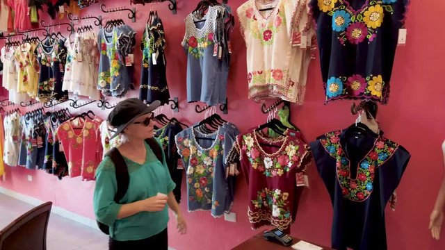 Mature woman tourist looking at huipil blouses in a store in Merida, Mexico.