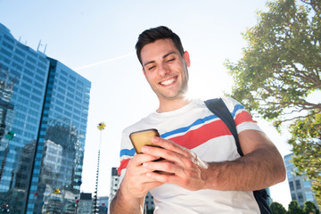 smiling young man walking in city looking at mobile phone