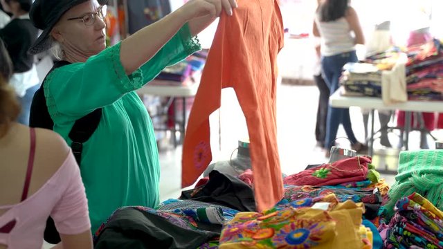 Mature woman looks at an orange huipil blouse in Merida, Mexico in an open air store.
