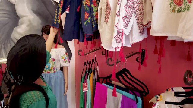 Mature woman looks at beautiful display of women’s huipil blouses in Merida Mexico store.