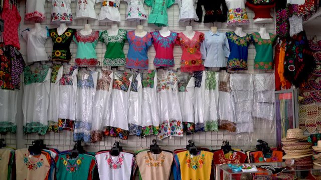Camera pans up in a store display of women’s Mexican ethnic blouses and dresses in a shop in Merida, Mexico.