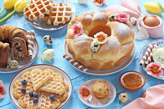 Easter festive dessert table with various of cakes, waffles, sweets and strawberry. Blue background. Overhead view