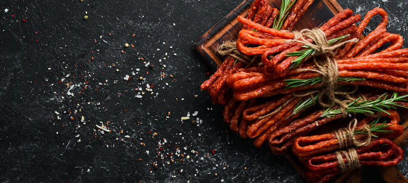 Smoked sausages on a black stone background. Kabanosy. Top view. Free space for your text.