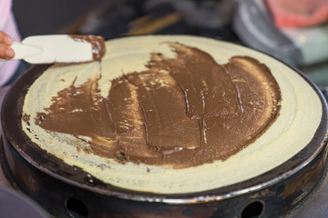 Thai pancakes preparation: smearing and spreading chocolate paste on pancakes fried on a pancake maker. delicious and affordable street food with local flavor
