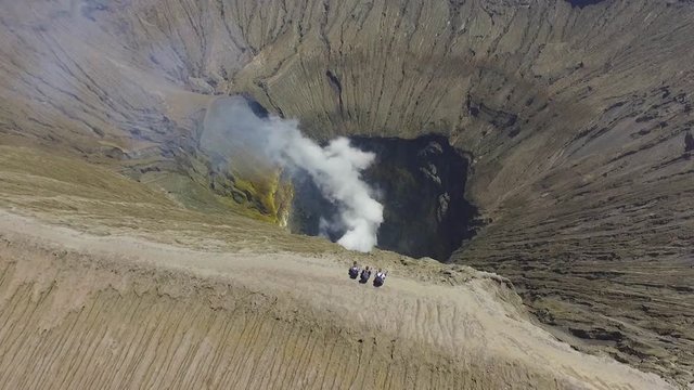 Aerial drone view of backpackers sitting alone at the crater edge of Mount Bromo, active volcano in Bromo Tengger Semeru National Park, East Java, Indonesia.