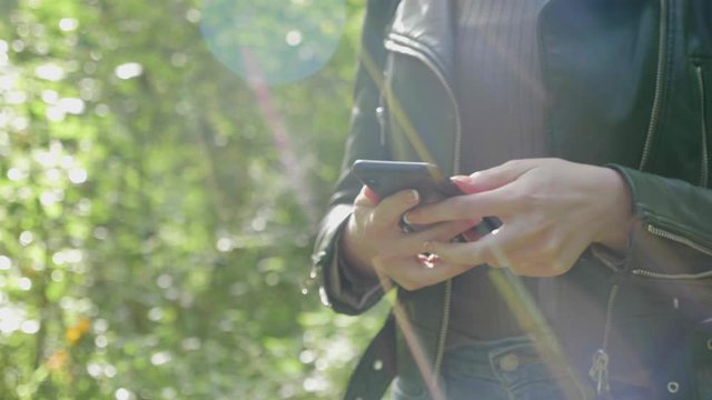 Stylish adult female hands holding smartphone in woods, tracking close-up