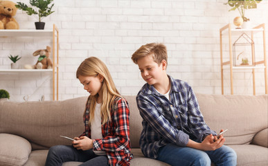 Curious Brother Reading Sister's Messages On Phone Sitting On Couch