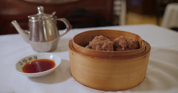 Tea & dim sum on a white table : Iron kettle, Dim Sum bambou basket steamed beef balls. Drinking and eating. Beautiful typical historic interior chinese restaurant, Luk Yu Tea House, Hong Kong.