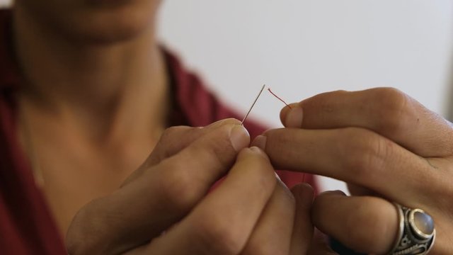 Middle eastern woman trying to thread unsuccessfully a red thread In The eye Of A needle. Close up. 4K