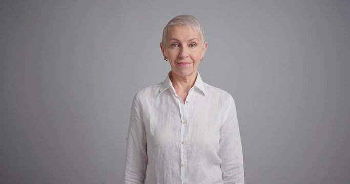 Portrait of a happy elderly woman standing on gray background and smiling