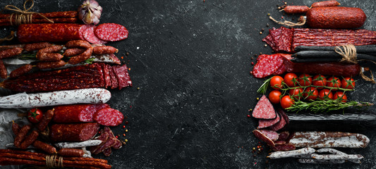 Background of salami, sausages and meat products, on black stone background. Top view. Free space...
