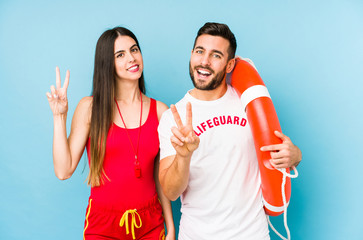 Young lifeguard couple isolated joyful and carefree showing a peace symbol with fingers.