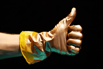 Image of gold painted Like gesture of hand in yellow rubber glove on black background