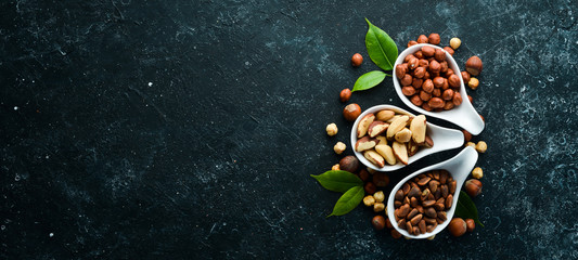 Assortment of nuts: pistachios, hazelnuts, pine nuts on a black stone background. free space for your text. Top view.