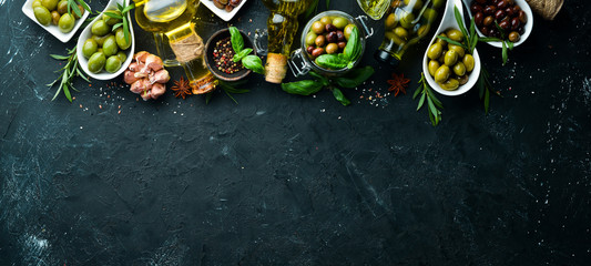 Olive oil, olives and spices on a black stone background. Top view. Free space for your text.