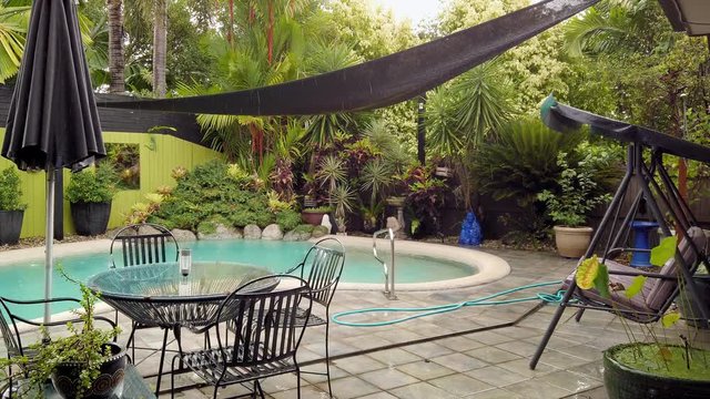 A beautiful outdoor pool surrounded by lush, green plant life in Queensland, Australia on a rainy day - Wide shot