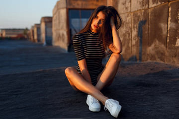 Female model with straight hair, seated on a roof, looking at sunset background. Closeup beauty portrait of young woman.