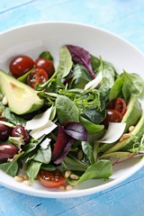 Green salad with avocado, tomatoes, olives and parmesan. Light blue background