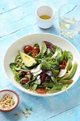 Green salad with avocado, tomatoes, olives and parmesan. Light blue background