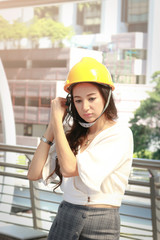 Outdoor portrait of beautiful pretty female engineer wearing yellow safety helmet standing and posing outdoors in modern city, elegant woman walking at city street