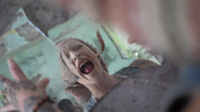 A young woman looks upset and sad into two broken pieces of a mirror and then hits her hands against it in anger, making one of them crack.