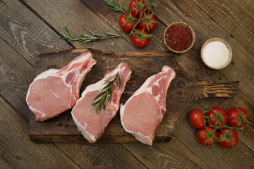 fresh raw pork meat isolated on a wooden cutting board and tomatoes and spices on a rustic wooden background. Flat lay. Top view. 