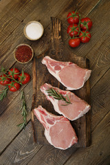fresh raw pork meat isolated on a wooden cutting board and tomatoes and spices on a rustic wooden background. Flat lay. Top view. 