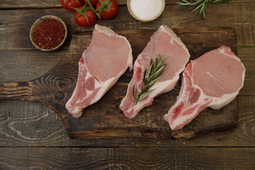 raw pork loin or sliced meat isolated on a wooden cutting board and tomatoes and spices on a rustic wooden background. Flat lay. Top view. Copy space.