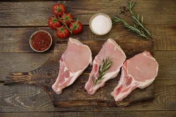 raw pork loin or sliced meat isolated on a wooden cutting board and rosemary, tomatoes, pepper, garlic, salt on a rustic wooden background. Flat lay. Top view.