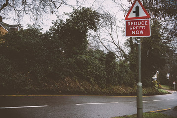 Reduce Speed sign on an empty urban street on a rainy day , old vintage style - 320303338